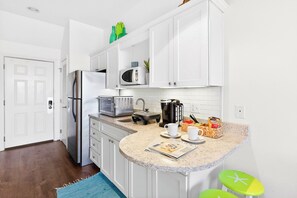 Cocina compacta con armarios blancos, microondas, cafetera y una pequeña isla con taburetes.