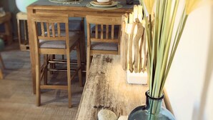 Una mesa de madera con sillas, un florero con plantas secas y un espejo en la pared.