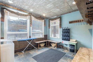 A laundry room with a bench, ironing board, and a drying rack.