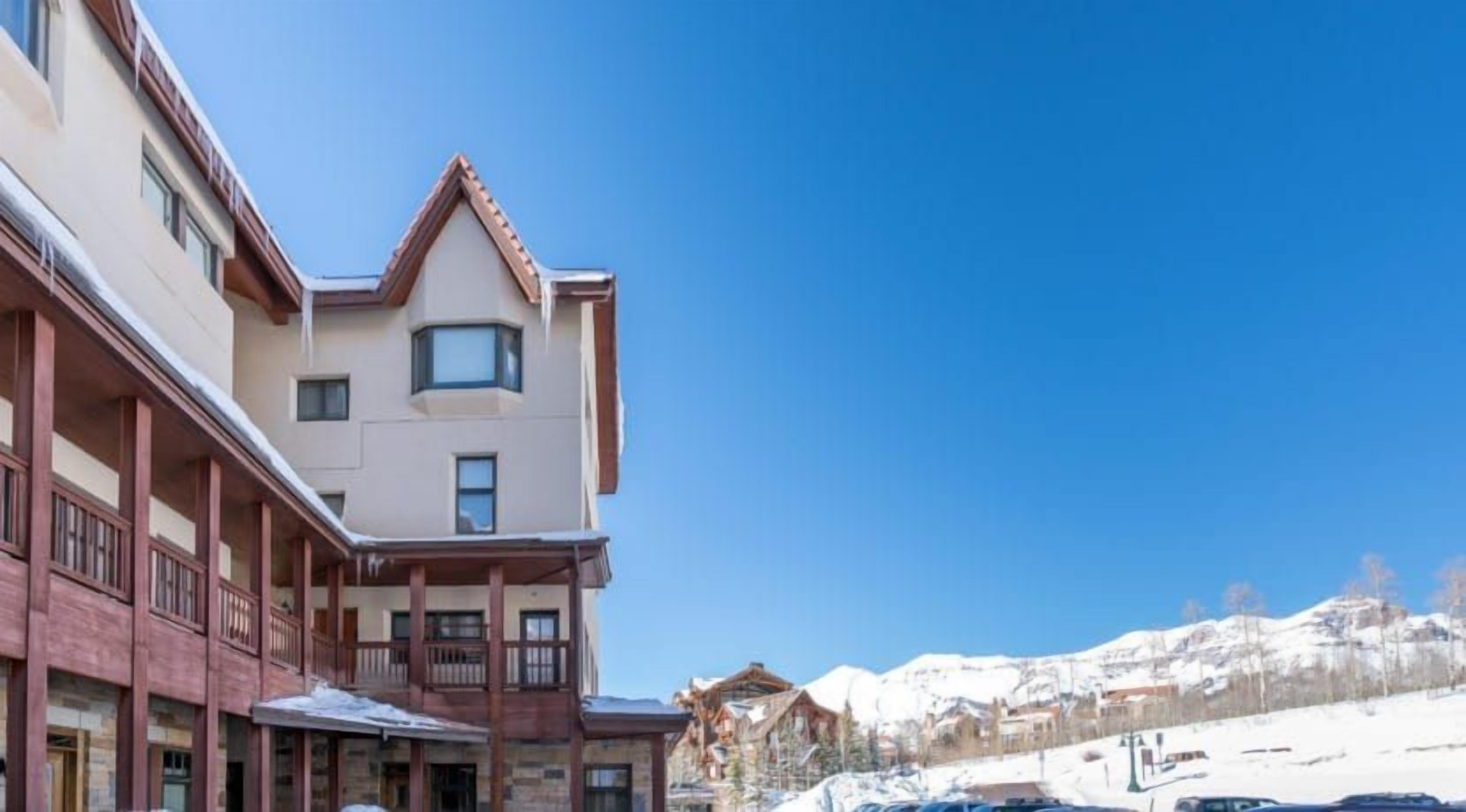 Un hôtel au style architectural traditionnel, doté d’un balcon remarquable et offrant une vue sur les montagnes en arrière-plan.