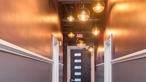 A hallway with a patterned floor, a black door with a window, and multiple hanging pendant lights. - N. Lexington Ave 1 BD King / 1 BA 566 SF + free parking (Asheville)