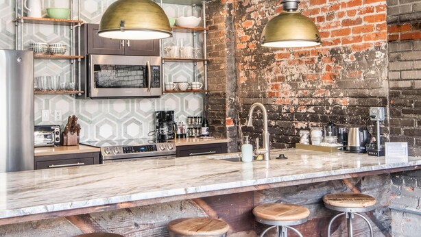A kitchen with a brick wall, stainless steel appliances, and a bar area with stools. - N. Lexington Ave 1 BD King / 1 BA 566 SF + free parking (Asheville)