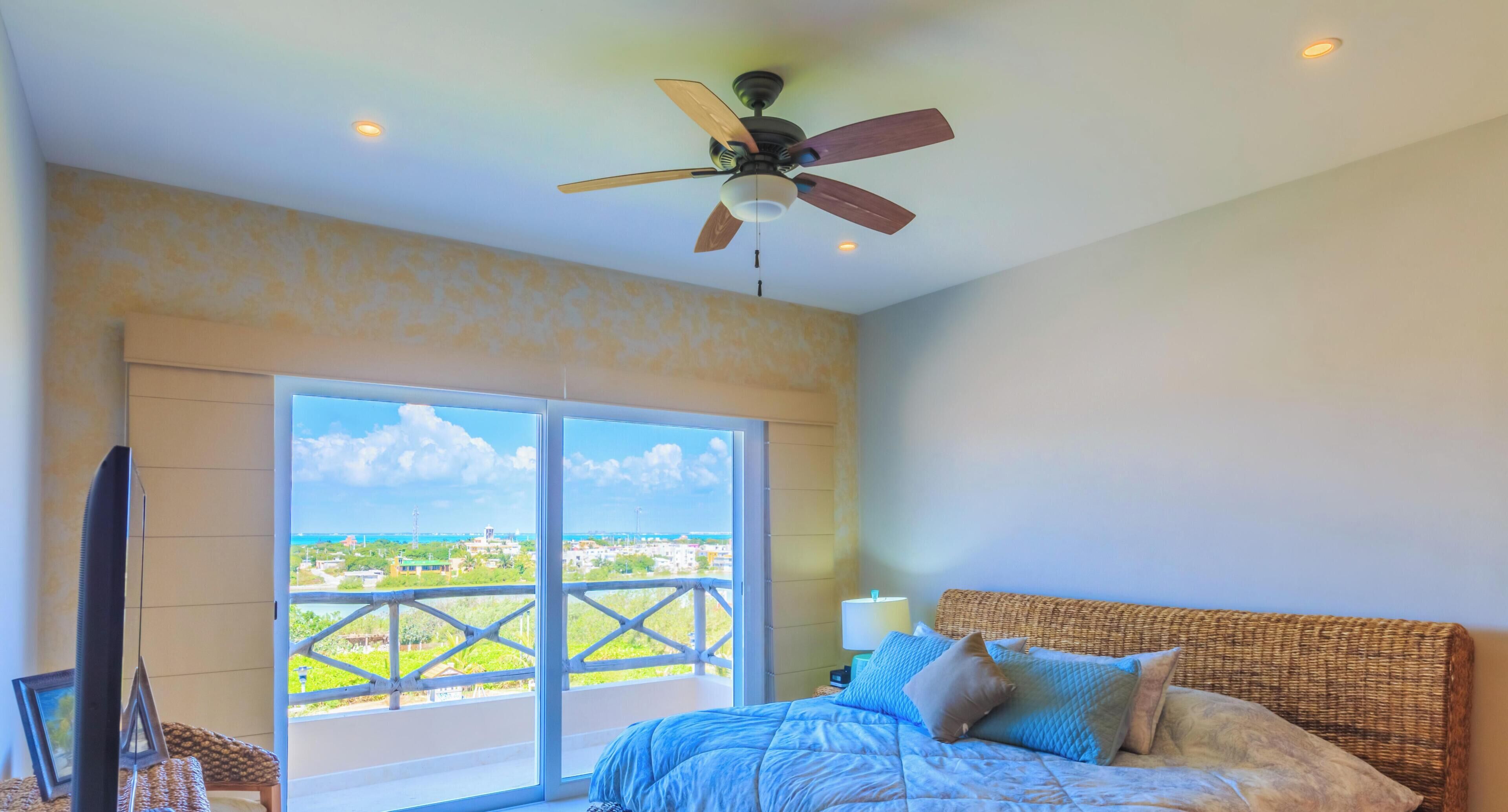 Un dormitorio con cama, ventilador de techo, televisión y balcón con vistas.