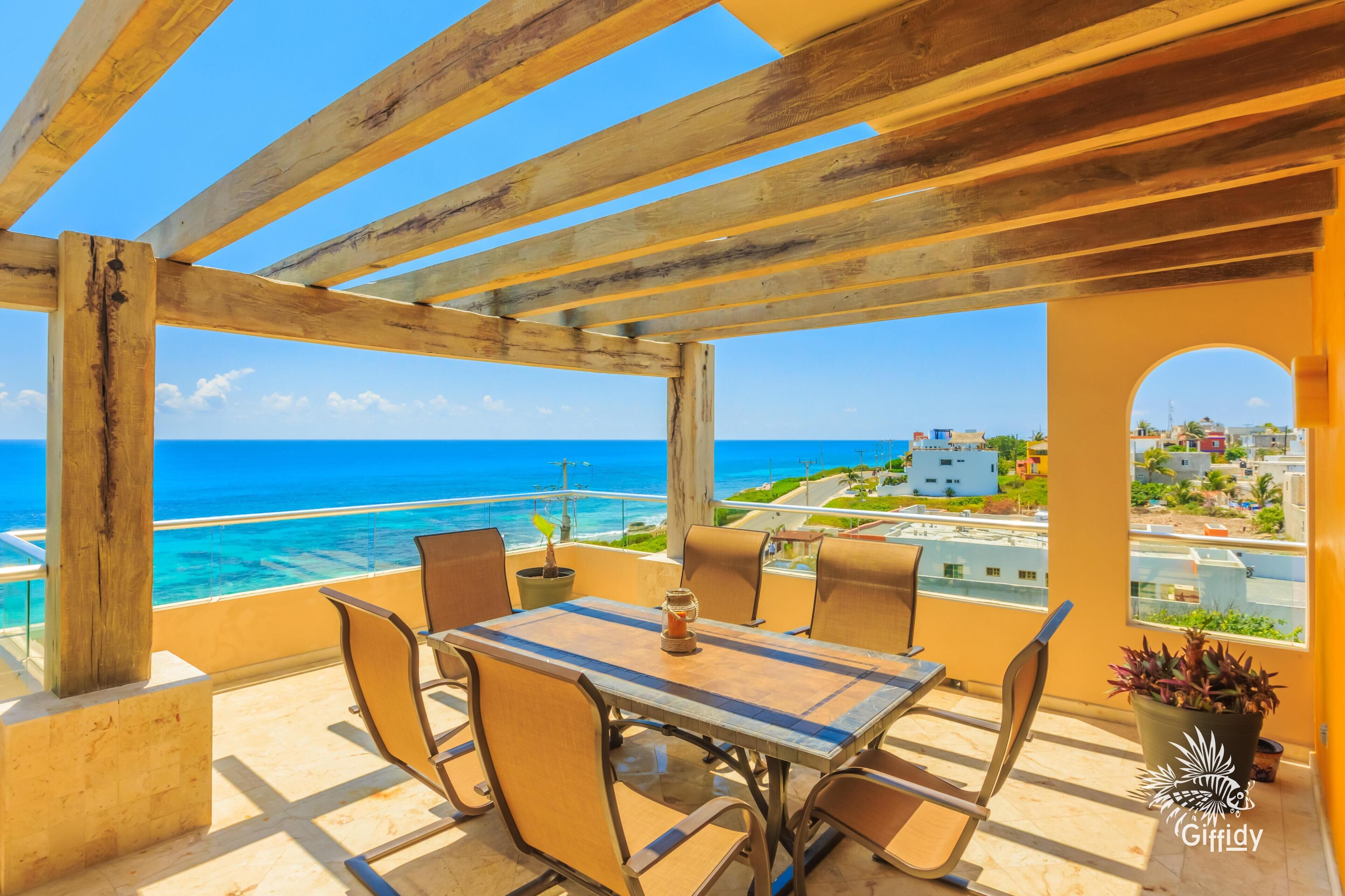 A wooden pergola with a table and chairs overlooking a coastal view.
