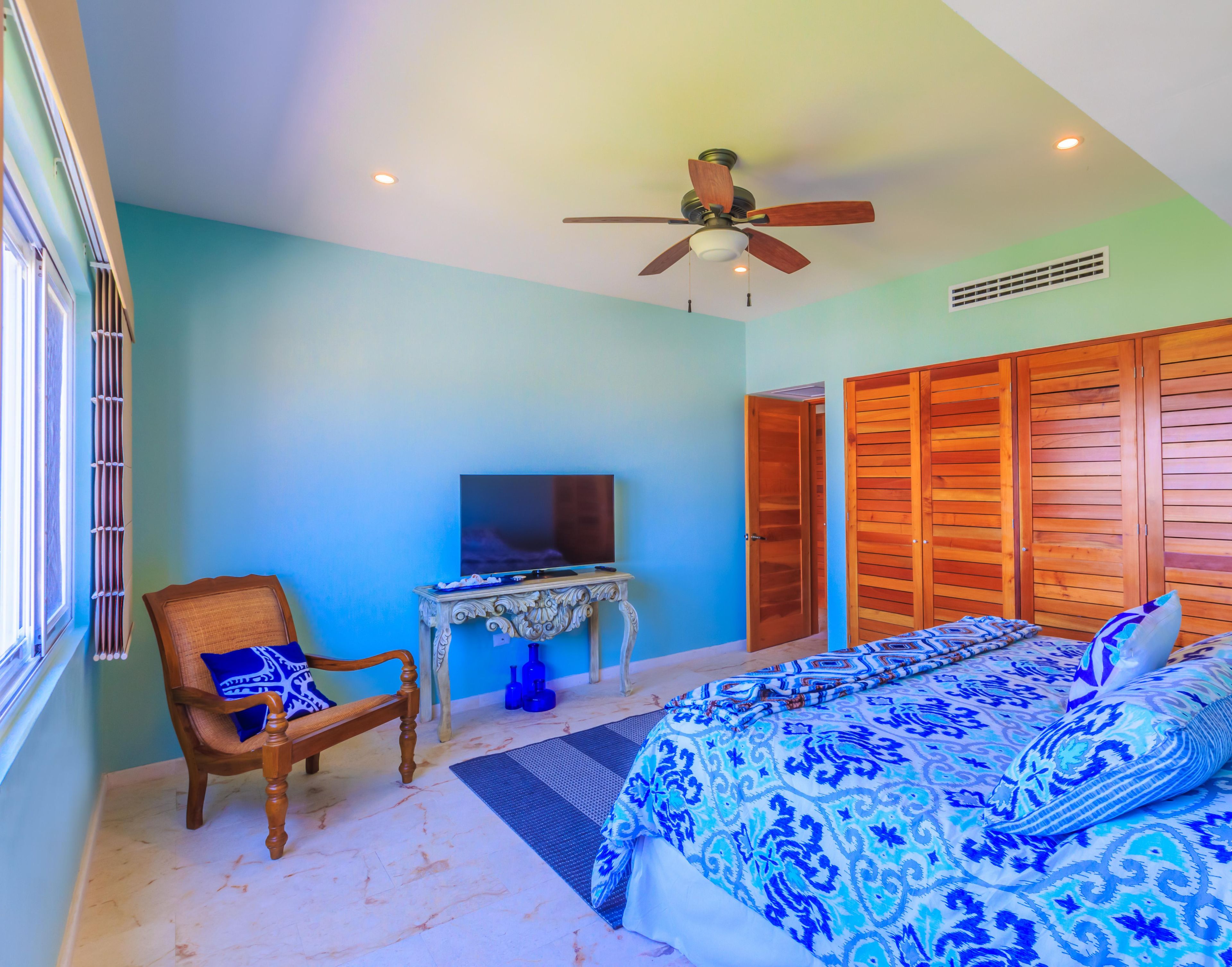 A bedroom with a bed, a chair, a television, and wooden closets.