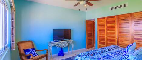 A bedroom with a bed, a chair, a television, and wooden closets.