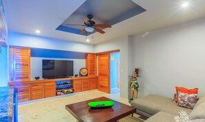 A living room with a TV, wooden cabinets, a ceiling fan, and a sofa. - Luxury. 4 BR PH Ocean View + Private Pool (Isla Mujeres)