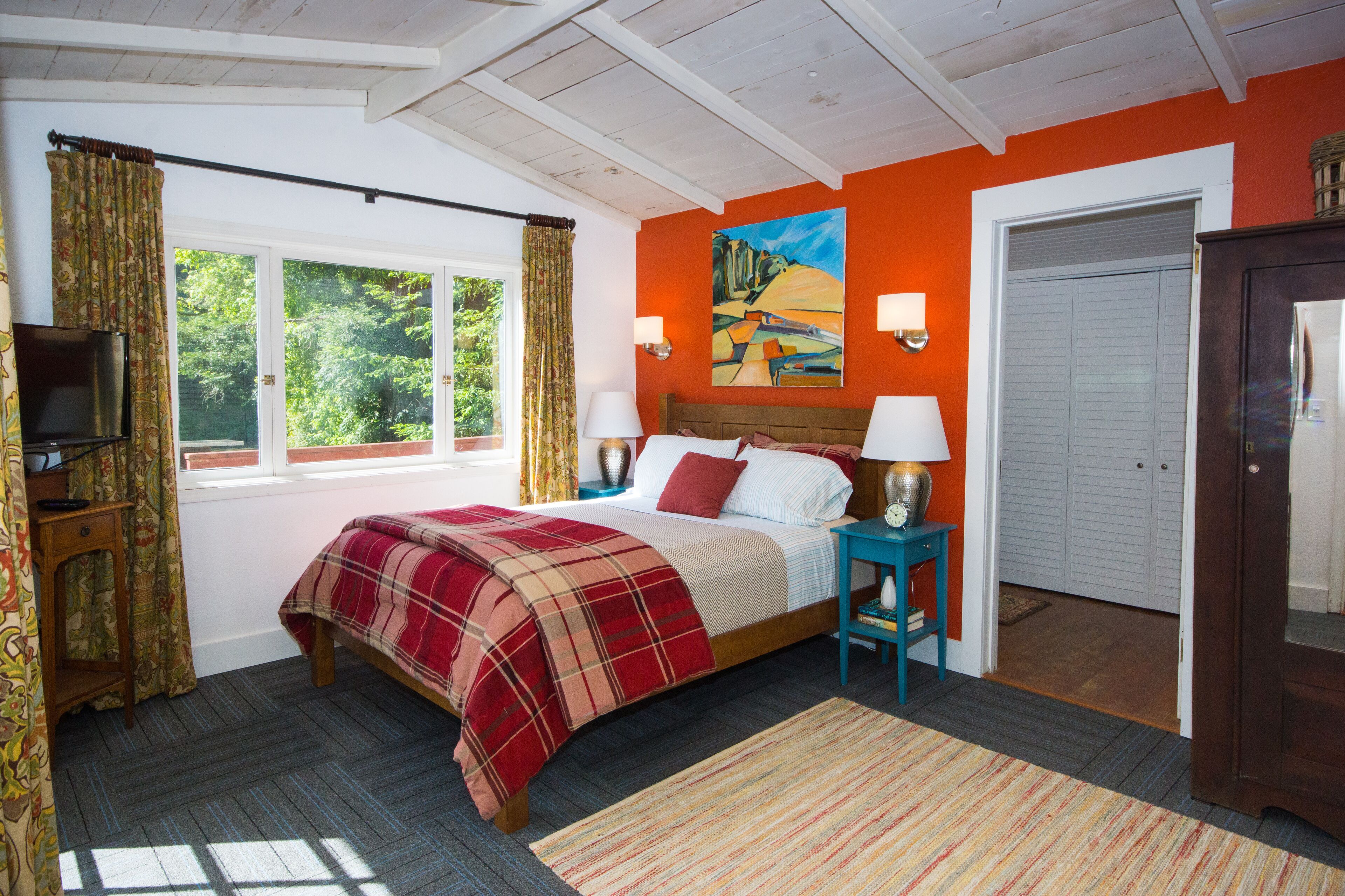 A bedroom with a bed, a television, a painting, and a door.