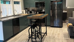 Une cuisine moderne avec des meubles de couleur sombre, des appareils en acier inoxydable et un îlot central en bois doté de tabourets.