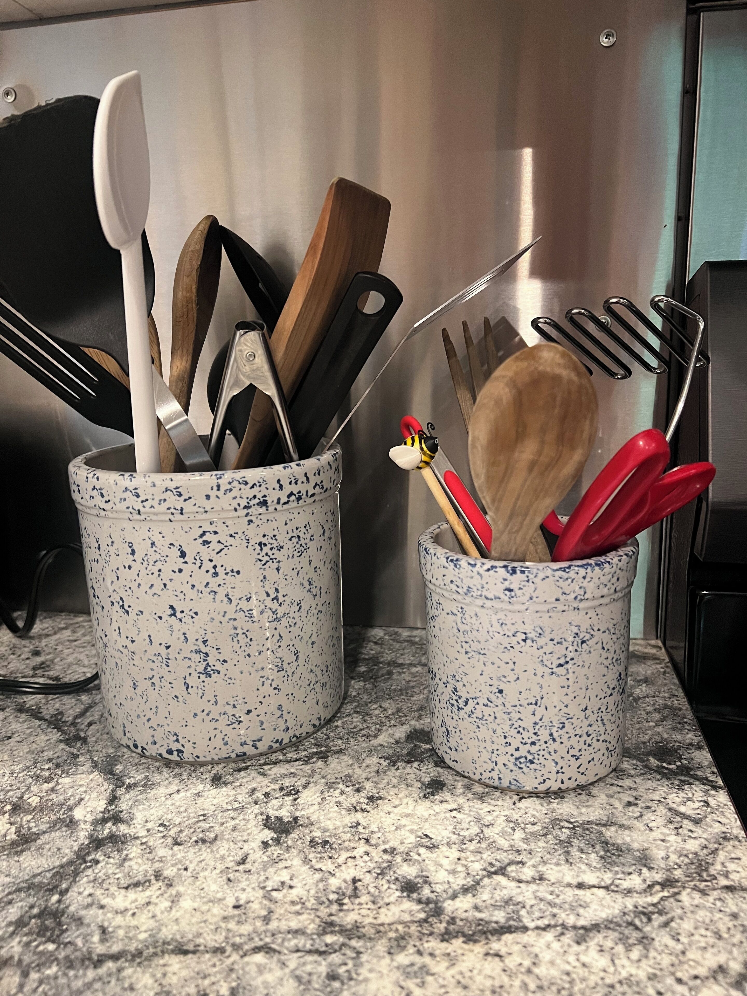 Dos soportes para utensilios de cocina sobre una encimera de granito.