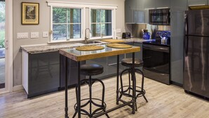 A modern kitchen with a central island, stainless steel appliances, and a window overlooking greenery.