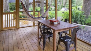Une terrasse en bois avec une table et des chaises, un hamac et une vue sur un jardin et une maison.