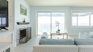 Una sala de estar con sofá, televisor, chimenea y vistas al mar a través de amplios ventanales.