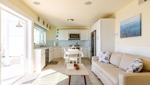 Una cocina moderna con armarios blancos, un microondas y un refrigerador. Hay una zona de comedor con una mesa y sillas, y un sofá beige con almohadones estampados de estrellas.