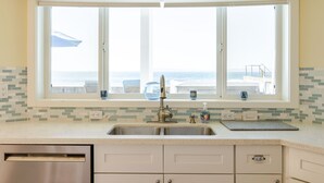 Una cocina con un ventanal grande, un lavamanos de acero inoxidable y un lavavajillas.