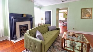A living room with a green sofa, a fireplace, a ceiling fan, and a glass coffee table. - Jones Green Room Loft Apartment -Dog Friendly Upon Approval! (Savannah)