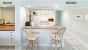 A kitchen with white cabinets, a central island with two bar stools, and a refrigerator.