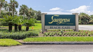 A sign for Sawgrass Beach Gate, a private community, with palm trees and a well-maintained garden in the foreground.