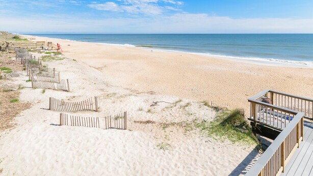 A beach with a wooden boardwalk, sandy beach, and a clear sky.