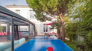 Une table de ping-pong dans une cour intérieure, protégée par une paroi en verre, entourée de verdure et avec un bâtiment en arrière-plan.