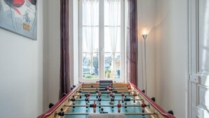 Ein Kicker steht in einem Raum mit einem großen Fenster, Vorhängen und einem Gemälde an der Wand.