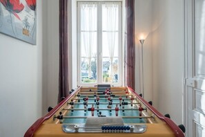 Ein Kicker steht in einem Raum mit einem großen Fenster, Vorhängen und einem Gemälde an der Wand.
