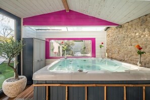 Un bain à remous avec vue sur un jardin et un mur en pierre.