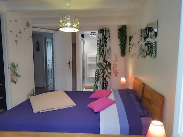 Une chambre à coucher avec un lit, des oreillers, une lampe de chevet et une porte donnant sur une autre pièce.