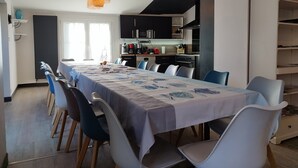 Un espace repas moderne avec une longue table, des chaises et une cuisine en arrière-plan.