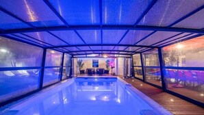 Ein beheiztes Hallenbad mit Glasverkleidung, einer Holzterrasse und Sitzgelegenheiten.