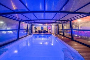 Ein beheiztes Hallenbad mit Glasverkleidung, einer Holzterrasse und Sitzgelegenheiten.