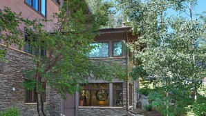 A two-story building with a stone facade, large windows, and a well-maintained garden with rocks and trees. - Mountain-Chic Chalet | Aspenwood #KA | 2B/2B (Snowmass Village)
