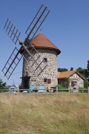 A stone windmill with a red roof, surrounded by a fence and a small building with a similar roof. - Windmill gite unusual (Auvergne)