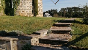 A stone tower with a windmill, stone steps leading up to a paved area, and a grassy field. - Windmill gite unusual (Auvergne)