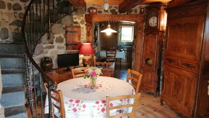 A rustic dining area with a round table, chairs, and a vase of flowers. A staircase with a metal railing is visible to the left. - Windmill gite unusual (Auvergne)