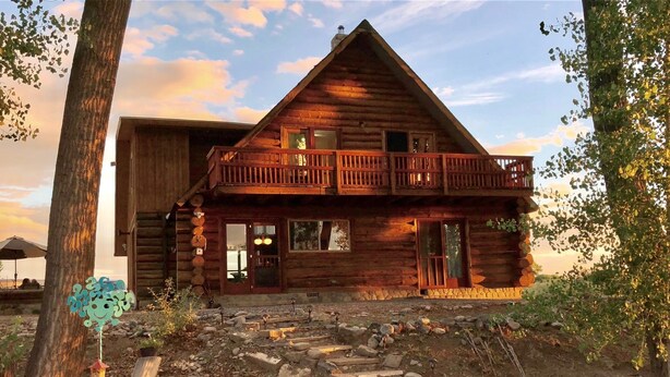 A log cabin with a balcony, a stone pathway, and a chair.