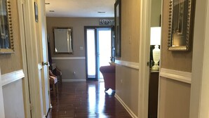 Un pasillo con suelo de madera, una puerta a la izquierda, una silla y una lámpara a la derecha.