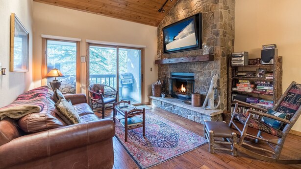 A cozy living room with a stone fireplace, leather sofa, and a bookshelf. - 3/2 Ski In/Out  BEAVER CREEK, steps to Village, Townsend Place A307 (Beaver Creek)