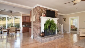 A spacious living room with hardwood flooring, a brick fireplace, and a television mounted above it. - "Historical”Yellow TeaCup Cottage,Farm setting, horses &goats ,rest n relax  (Rockford)