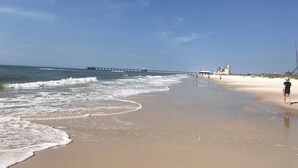 A beach with a pier extending into the ocean, sandy shore, and a few buildings in the background.