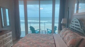 A bedroom with a large bed, a dresser, and a view of the beach through a balcony.