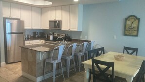 A modern kitchen with white cabinets, a stainless steel refrigerator, a microwave, and a granite island with bar stools.