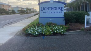 A sign for Lighthouse Condominiums with a clear road and buildings in the background.