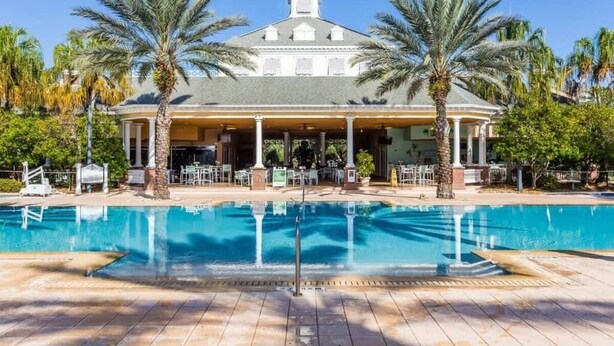 A pool with a building in the background, palm trees, and a clear sky.