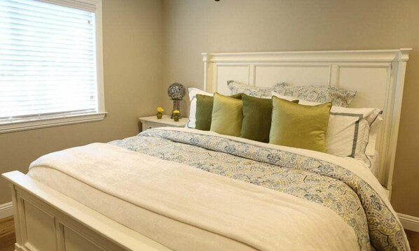 A bedroom with a bed, a nightstand, a vase with flowers, and a window with blinds. - Upscale Pool/Jac House: 3 EnSuites, Walk to Disney (Anaheim)
