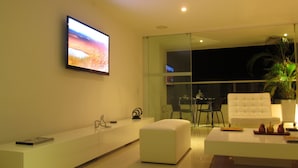 A modern living room with a flat-screen TV, a white sofa, a glass door leading to a balcony, and a potted plant. - Oceanfront Penthouse with Stunning Views of the Caribbean. (Cartagena)