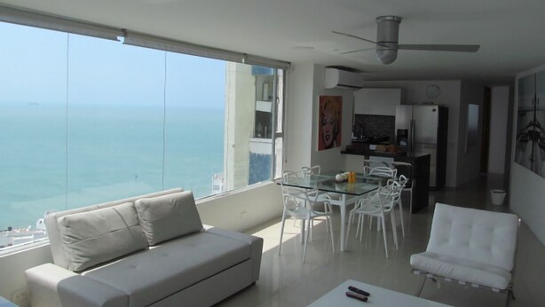 A modern living room with a large glass table, white chairs, a sofa, and a view of the ocean. - Oceanfront Penthouse with Stunning Views of the Caribbean. (Cartagena)