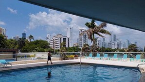 A swimming pool with lounge chairs and a city skyline in the background. - Oceanfront Penthouse with Stunning Views of the Caribbean. (Cartagena)