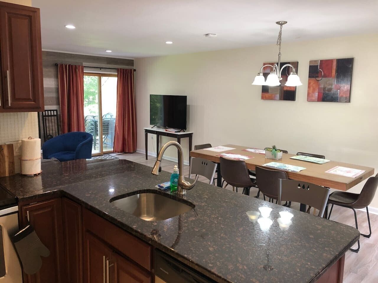 A modern kitchen with granite countertops, a stainless steel sink, and a dining area with a wooden table and chairs.