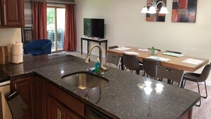 Een moderne keuken met granieten aanrecht, een roestvrijstalen spoelbak en een eethoek met een houten tafel en stoelen.
